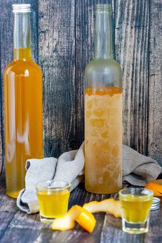 two bottles and glasses filled with liquid next to orange peels on a wooden table