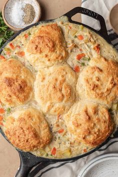 a skillet filled with biscuits and vegetables on top of a table next to plates