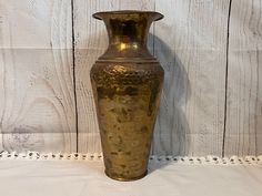 a gold colored vase sitting on top of a white tablecloth next to a wooden wall