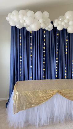 the table is set up with white and gold balloons on it, along with blue drapes