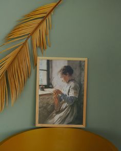 a painting hanging on the wall next to a plant and a framed photo with a woman's face