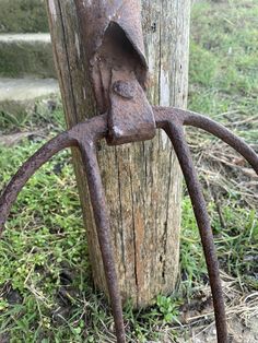 an old rusty piece of metal hanging from a wooden pole in the grass next to a tree