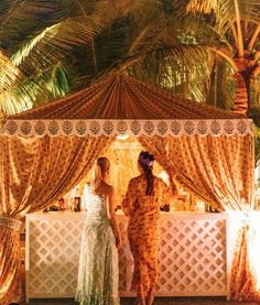 two women standing under a canopy in front of palm trees