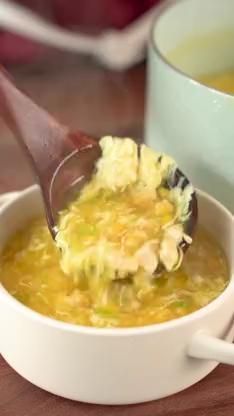 a bowl of soup is being stirred with a ladle on a table next to a cup