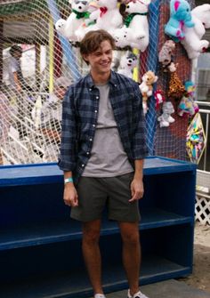 a young man standing in front of a carnival ride with stuffed animals hanging from the ceiling