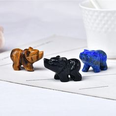 three small plastic animals sitting next to each other on a white tablecloth with a cup in the background