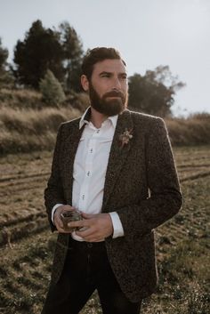 a man with a beard wearing a suit and holding something in his hand while standing on a field