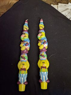 two yellow and blue candy shaped candles sitting on top of a black cloth covered table