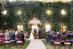 an outdoor wedding ceremony with the bride and groom standing at the alter surrounded by greenery