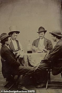 three men sitting at a table with one holding a bottle and the other wearing a top hat