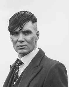 a black and white photo of a man in a suit with his hair pulled back