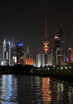 the city is lit up at night with lights reflecting in the water and skyscrapers