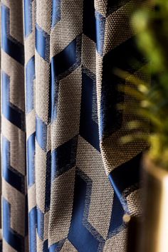 a close up view of a curtain with blue and grey geometric designs on it, next to a potted plant