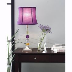 a purple lamp sitting on top of a table next to a vase filled with flowers