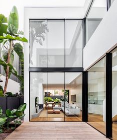 the inside of a modern house with glass walls and wood flooring is seen from outside