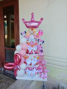 a pink and white birthday cake with balloons on the front steps, next to a door