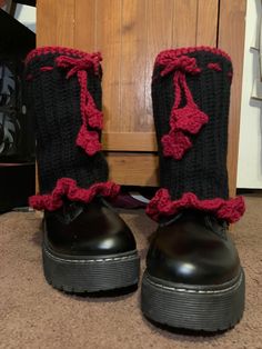 a pair of black and red knitted boots with bows on the side, sitting next to a wooden door