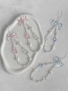 three pieces of jewelry are sitting on a white platter with pearls and bows hanging from it