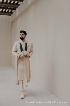 a man with a beard wearing a white suit and green tie standing next to a wall