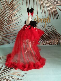 a red dress with black and white mickey mouse on the top, sitting in front of palm leaves