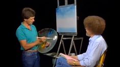 a woman sitting in front of a easel with a painting on it