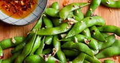 green beans are sitting on a wooden table next to a bowl of chili and seasoning