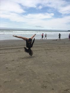 a person doing a handstand on the beach while others walk in the background