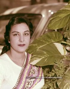 a woman standing in front of a car next to a green plant with leaves on it