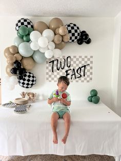 a little boy sitting on top of a bed next to balloons and a sign that says two fast