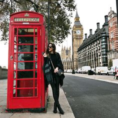 a woman standing next to a red phone booth on the side of a road with big ben in the background