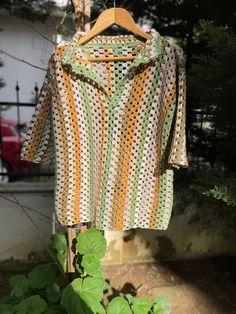 a crocheted shirt hanging on a clothesline in front of some trees and bushes