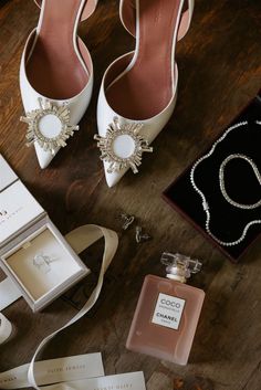 a pair of white high heeled shoes sitting on top of a wooden floor next to jewelry