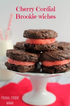 chocolate cookies with pink frosting are on a white platter next to a glass of milk