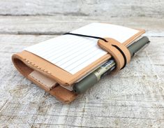 a notebook with a pen in it sitting on top of a piece of wood next to a clipboard