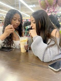 two young women sitting at a table eating and drinking milkshakes with straws