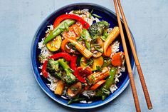 a blue plate filled with vegetables and rice next to chopsticks on a table