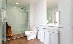 a white toilet sitting next to a walk in shower under a bathroom mirror on top of a wooden floor