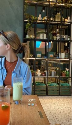 a woman sitting at a table with drinks in front of her and looking into the distance