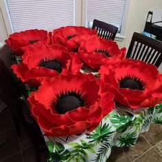 there are many large red flowers on the dining room table with chairs and a window in the background