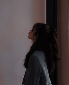 a woman standing in front of a window with her head turned to the side and looking out