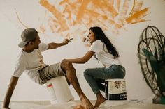 a man painting a woman's leg in an orange and white room with graffiti on the wall