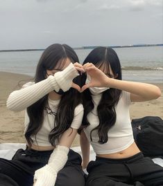 two young women sitting on top of a beach