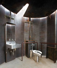 an industrial bathroom with stainless steel fixtures and toilet, sink, and shower stall in the corner