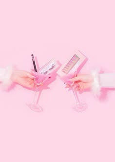 two hands holding wine glasses with pink nail polish and lipstick in them on a pink background