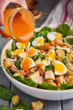 someone pouring dressing onto a salad with eggs and spinach leaves in a white bowl