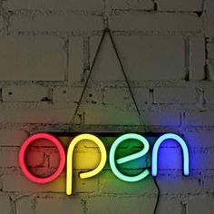 a neon sign that says open hanging on a brick wall