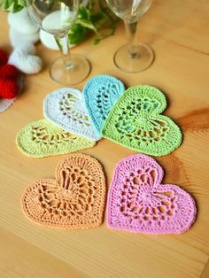 four crocheted hearts sitting on top of a table next to two wine glasses