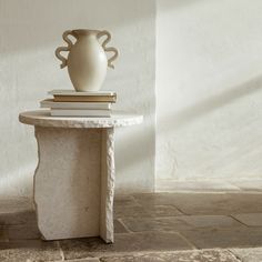 a white vase sitting on top of a table next to a stack of books in front of a wall