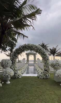 an outdoor ceremony setup with white flowers and greenery on the grass, surrounded by palm trees