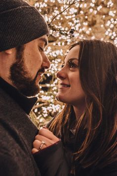 a man and woman standing next to each other in front of a tree with lights